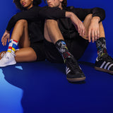 Two people sitting on a blue floor wearing colorful art-themed socks. thumbnail