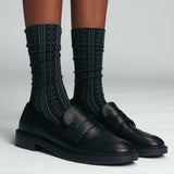 Black leather shoes with textured black pointelle socks on a light gray background thumbnail
