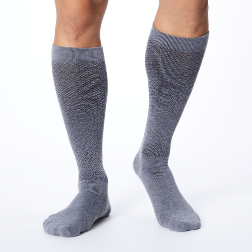 Front profile of a man wearing a pair of gray over the calf compression Dr. Scholl's socks.