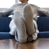 A person reclining on a blue couch with their feet up on a wooden table, wearing light gray textured socks with a raised bubble pattern on the soles.