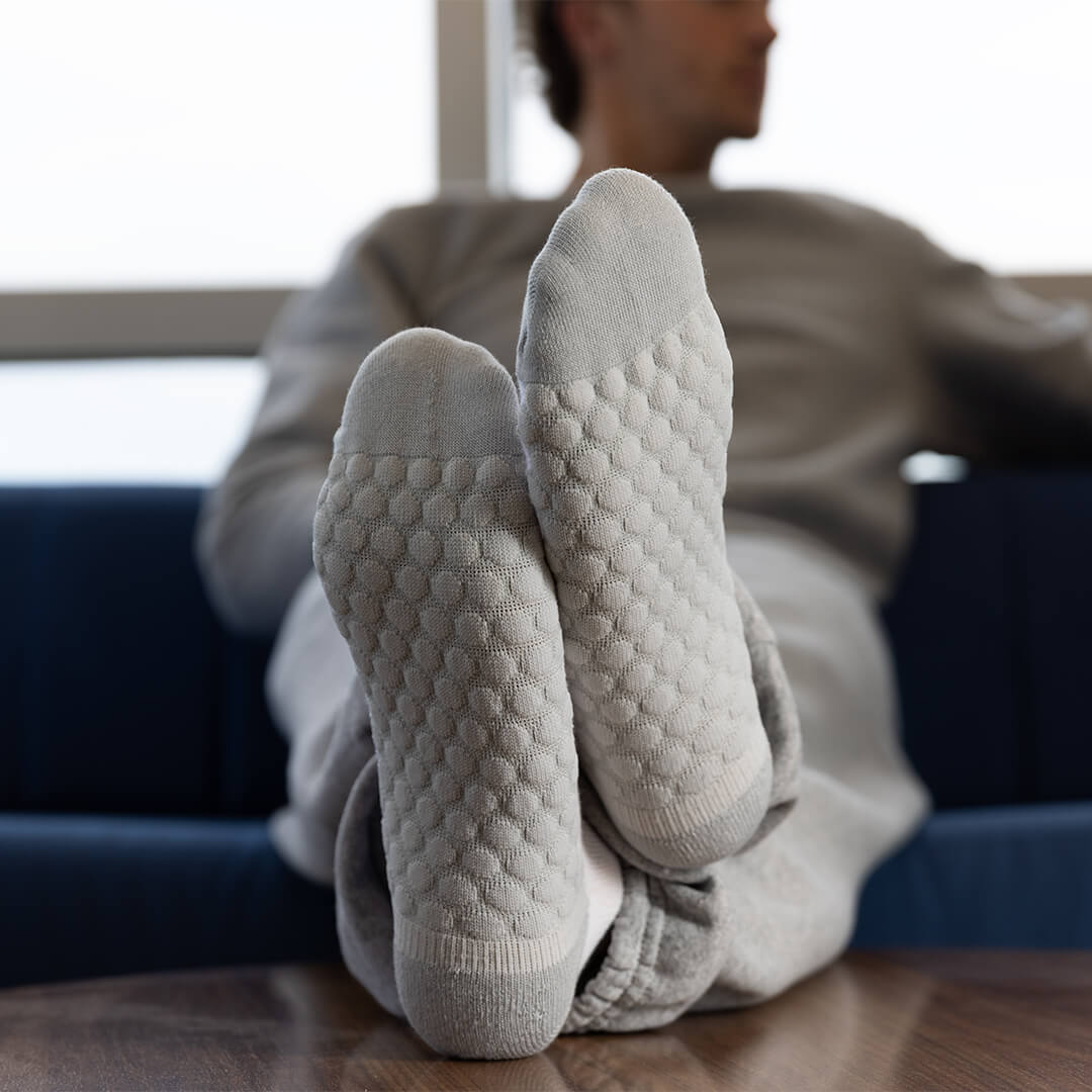A person reclining on a blue couch with their legs raised, wearing light gray textured knit socks and matching lounge pants in a bright indoor setting.