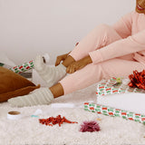 A woman sitting on a rug wearing fuzzy striped socks with Christmas decorations around her.