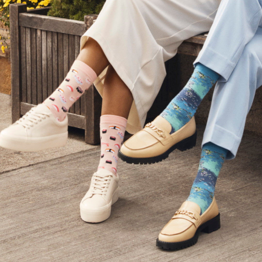Two women sitting on a bench wearing HOTSOX novelty socks.