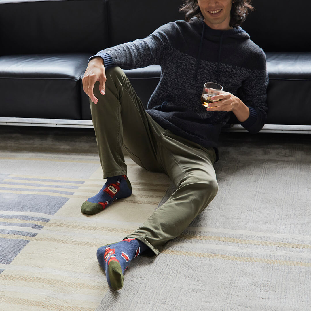 Person sitting on a couch wearing colorful socks and holding a glass.