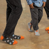 Two people wearing gray socks with colorful Halloween designs on a concrete floor.