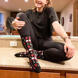 Person sitting on a counter wearing black tights and patterned socks with a wine design. thumbnail