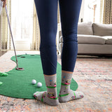 Person playing mini golf indoors with a green mat and golf ball on a patterned rug.