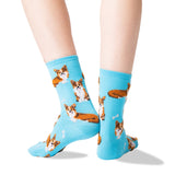 A pair of light blue crew socks with an all-over print of corgi dogs and small white bones, shown on a person's feet against a white background. thumbnail