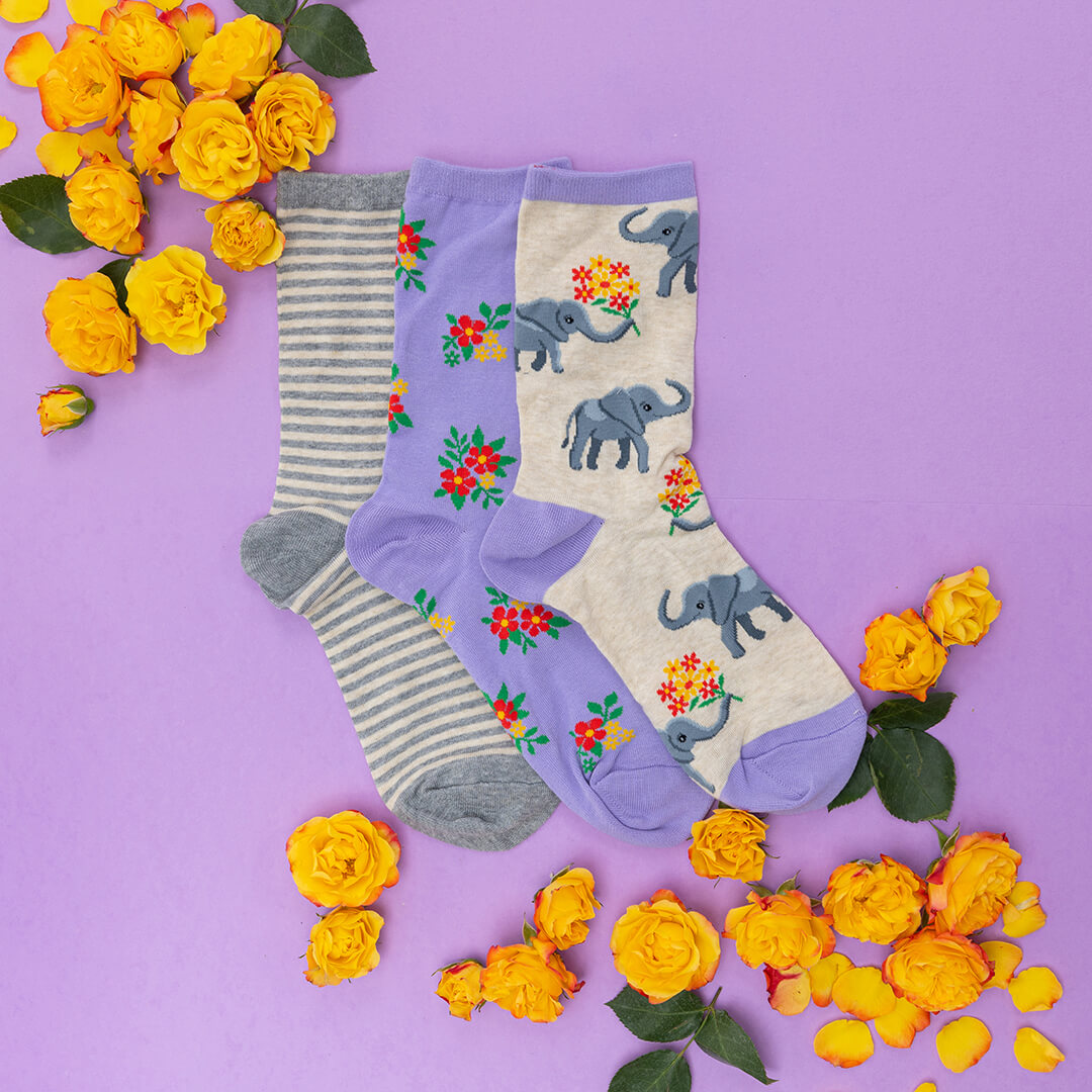 Three pairs of socks with elephant designs on a purple background with yellow flowers.