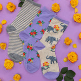 Three pairs of socks with floral and elephant designs on a purple background with yellow flowers.