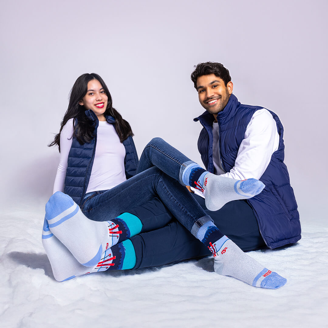 Two people sitting on a snowy surface wearing matching blue and gray socks.