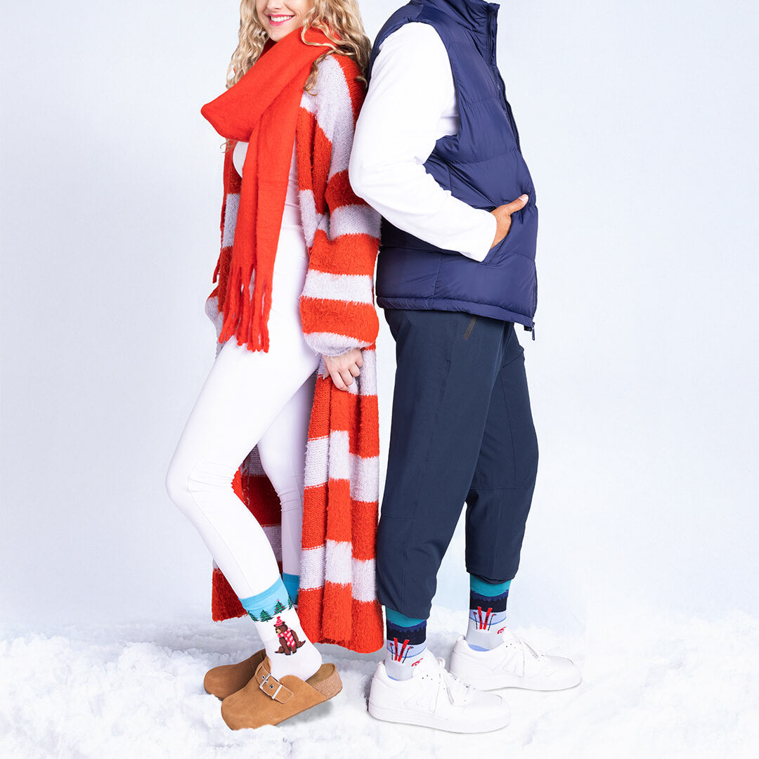 Two people standing in the snow wearing winter clothing with a red scarf and blue vest.