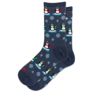 A pair of navy blue crew socks with a repeating pattern of penguins on ice, snowflakes, and small red accents.