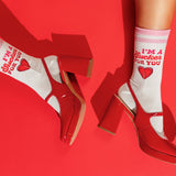 White crew socks with red text reading 'I'M A Sucker FOR YOU' and a red heart, worn with glossy red block-heel shoes against a bright red background. thumbnail