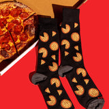 Black crew socks with a repeating pizza slice pattern, styled on a bright red background next to a sliced pepperoni pizza.