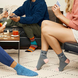 Gray ankle socks with a cat face design and pink toes, worn by a person sitting on a couch while playing cards in a cozy living room setting. thumbnail