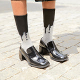 Black patent leather shoes worn with socks featuring a dripping design on a stone pavement.