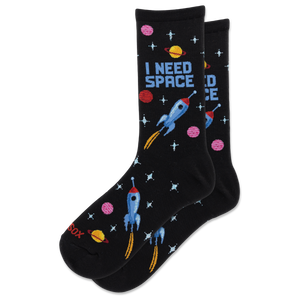 A pair of black crew socks with a colorful space-themed pattern featuring blue rockets, pink and yellow planets, and the text 'I NEED SPACE' on a white background.