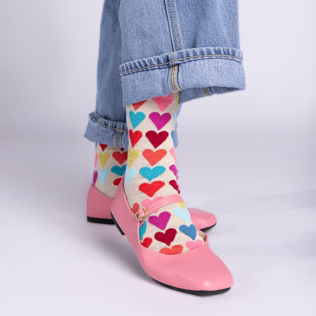 Colorful heart-patterned socks worn with pink shoes and blue jeans on a light gray background