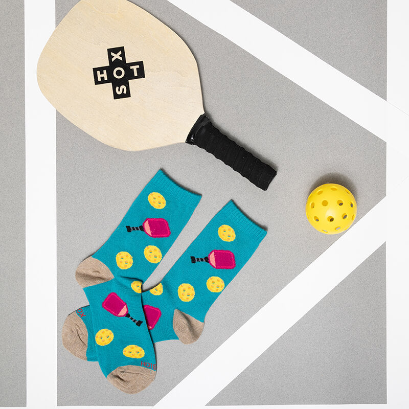 Blue socks with pink and yellow designs, a paddle, and a yellow ball on a gray background