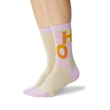 A pair of crew socks worn on a model's feet, featuring a heather beige body with a lavender ribbed cuff and toe, and a graphic design of the word 'SHOOK' in orange and pink. thumbnail