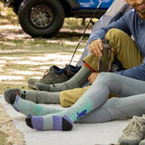 Two people sitting on a camping mat wearing colorful socks with 'Jeep' branding, next to a vehicle and tent.