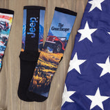 Two pairs of socks with Jeep-themed designs on a wooden surface next to an American flag. thumbnail
