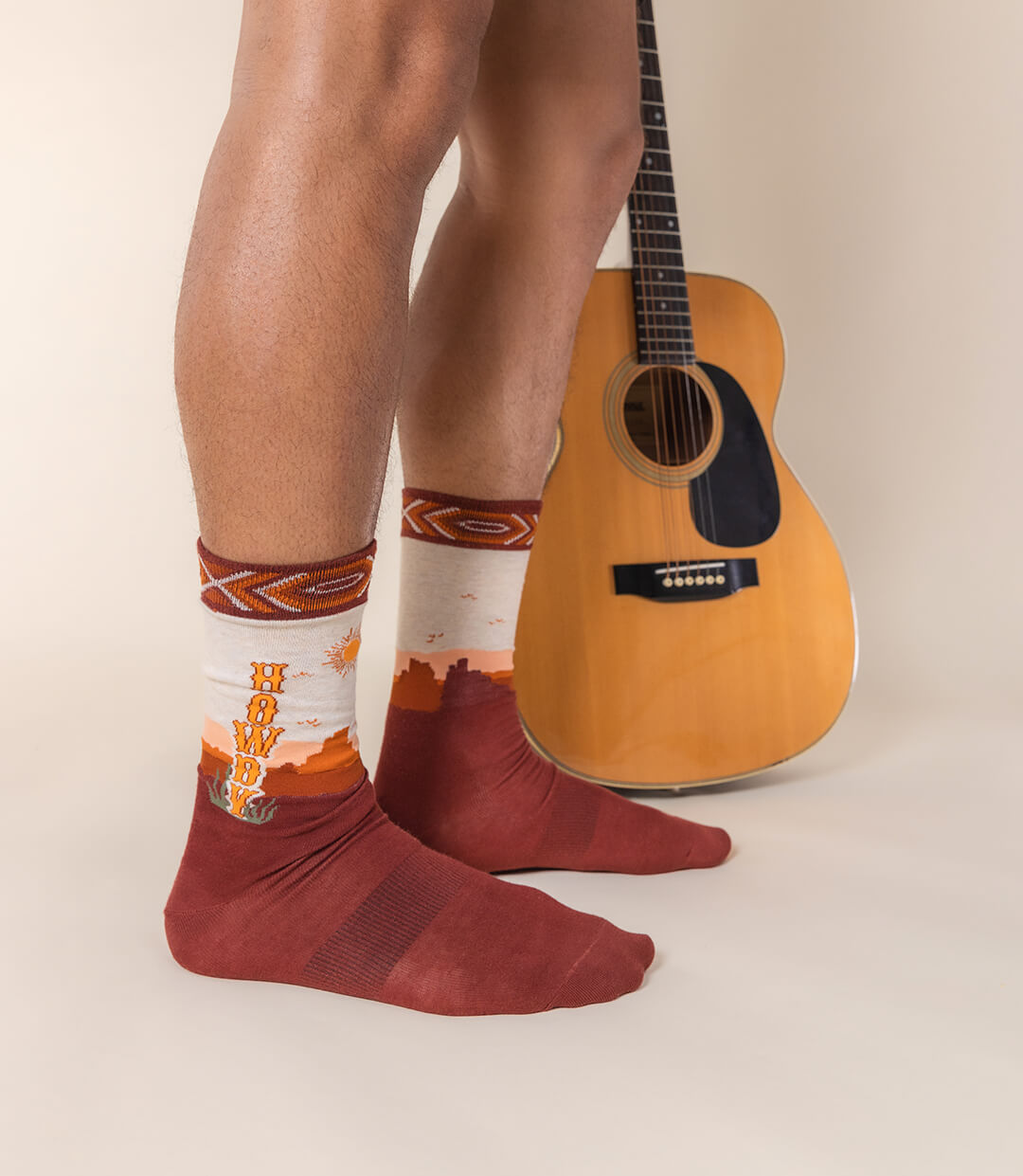 Person wearing patterned socks with a guitar on a neutral background