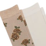 A close-up of a beige sock with a woven rose pattern, brown toe and heel, and another pair of light cream socks. thumbnail
