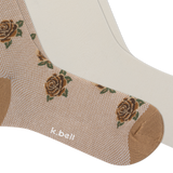 A close-up of a beige sock with a woven rose pattern, brown toe and heel, another pair of light cream socks, and the brand name 'k.bell' printed near the ankle. thumbnail