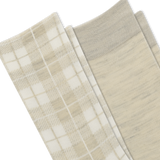 Close-up of folded socks in a soft neutral palette, showing a plaid pattern in cream and beige on one sock and a solid heathered light beige on the other, with a ribbed cuff.