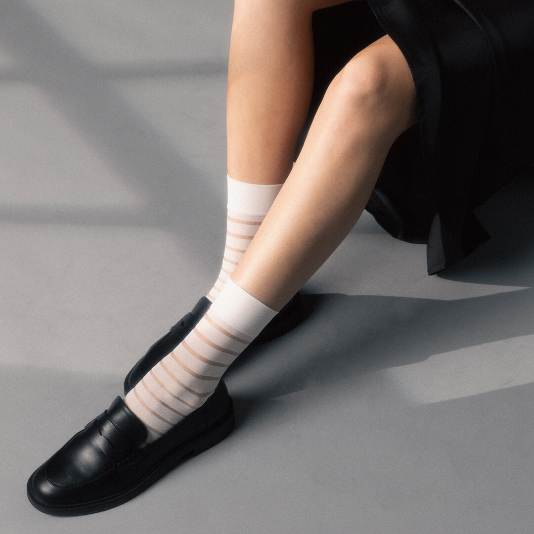 Person wearing white striped socks with black shoes on a gray surface