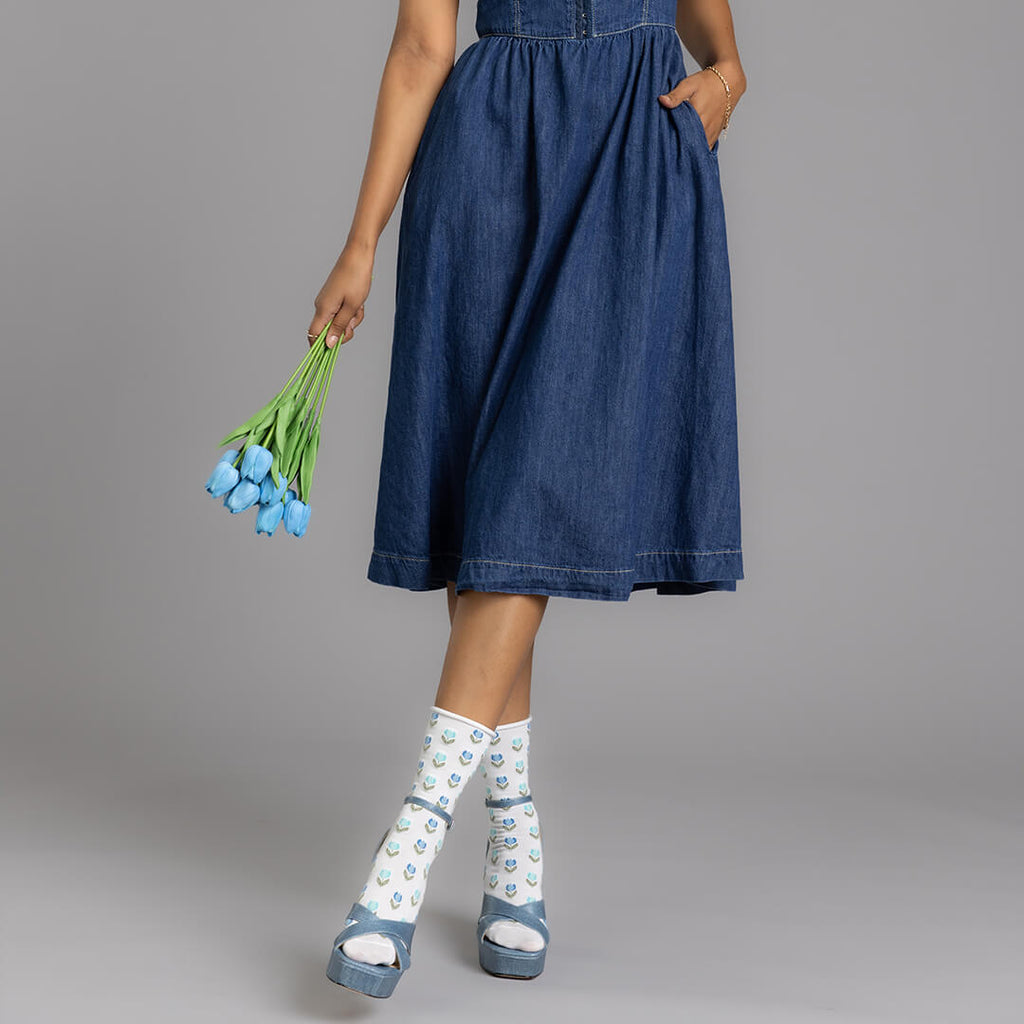 Person wearing a blue denim dress holding blue tulips on a gray background