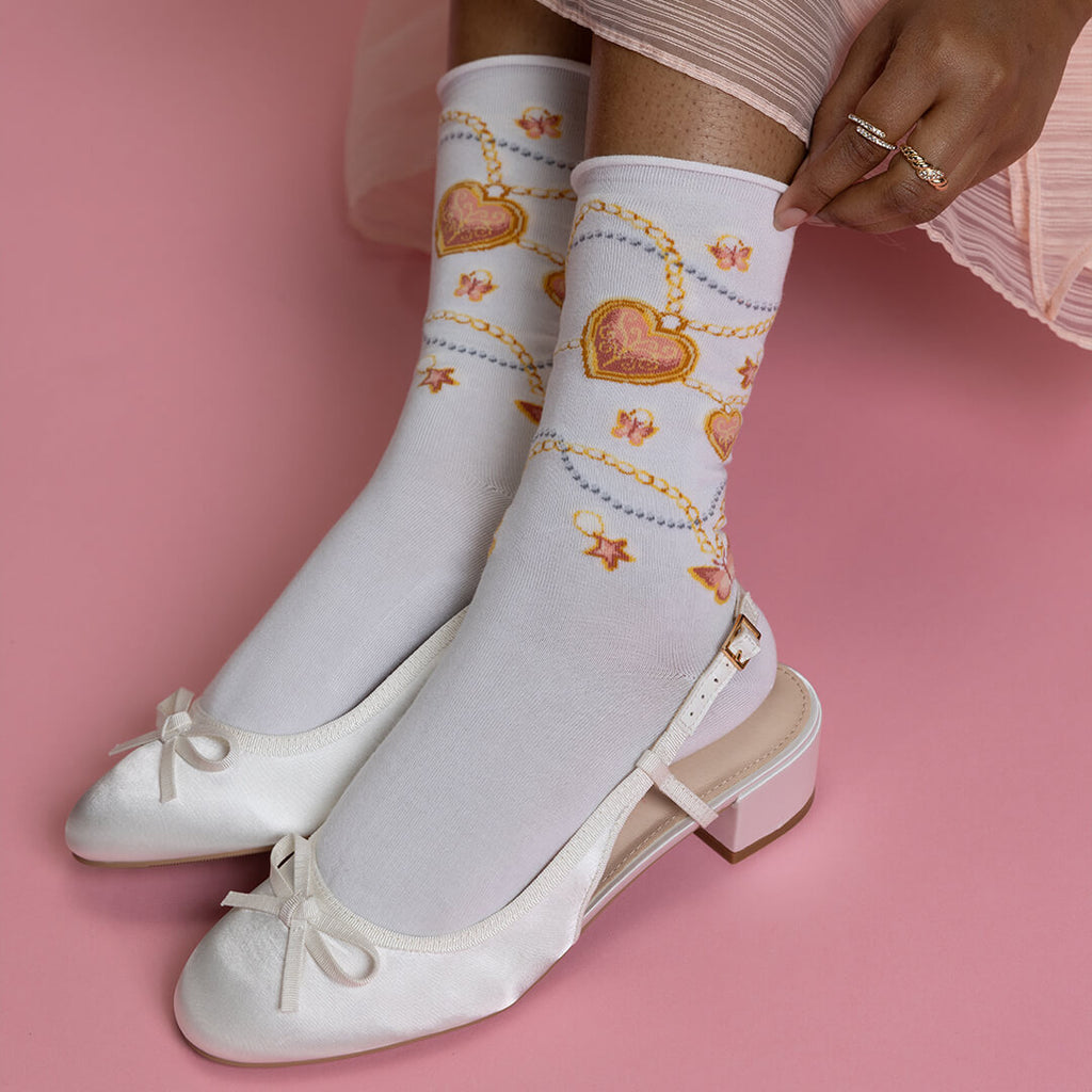 White socks with heart and chain design worn with white shoes on a pink background