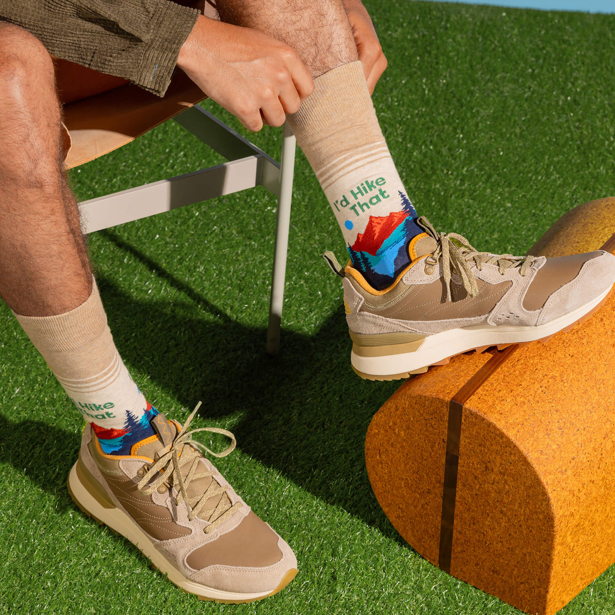 Detail shot of a man in a camping scene, wearing hiking shoes, a textured corduroy shirt, and HOTSOX crew socks with a knit camping scene and the phrase 'I'd Hike That.'