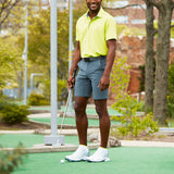 Man in yellow shirt and gray shorts holding a golf club on a putting green.
