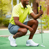 Man in a yellow shirt and gray shorts crouching on a golf course holding a golf club. thumbnail