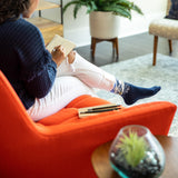 Person sitting on an orange chair in a living room, holding a notebook.
