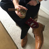 Person sitting on a chair wearing brown leather shoes and dark pants, holding a glass with a cigar. thumbnail