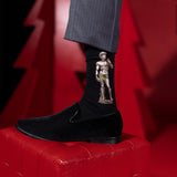 Black sock with a graphic design of a muscular figure holding a flower, worn with a black shoe on a red surface.