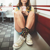 Person sitting in a diner wearing colorful socks and white sneakers, holding a drink. thumbnail