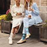 Two women sitting on a bench outdoors, wearing colorful socks. thumbnail