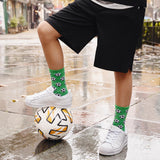Person balancing on a soccer ball with green socks featuring black patterns, standing on a wet pavement. thumbnail