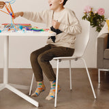 Child sitting at a table playing with colorful toys in a room with a couch and flowers. thumbnail