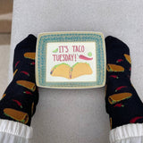 Person wearing taco-themed socks with a decorative plate saying 'It's Taco Tuesday' on a gray surface. thumbnail