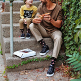 Man and child sitting on steps eating pizza, surrounded by greenery. thumbnail