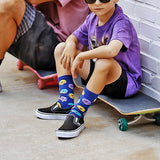 Child sitting on a skateboard wearing colorful socks with a brick wall background thumbnail