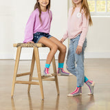 Two children wearing colorful socks and standing on a wooden floor. thumbnail