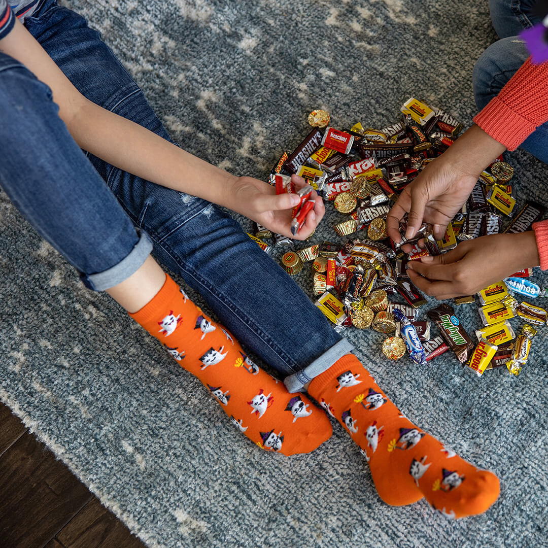 Kids wearing orange socks with Halloween patterns, sitting on a carpeted floor with candy bars.