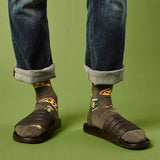 Person wearing sandals, rolled-up jeans, and patterned beer and pizza slice socks on a green background thumbnail